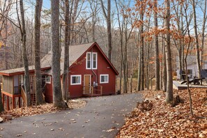 Une cabane rouge avec un porche à l’avant, entourée d’arbres et dotée d’une terrasse couverte.