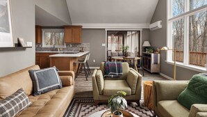 Un espacio habitable amplio con un sofá, sillones y una mesa de centro. Se ve una cocina con armarios de madera y un comedor con mesa y sillas.