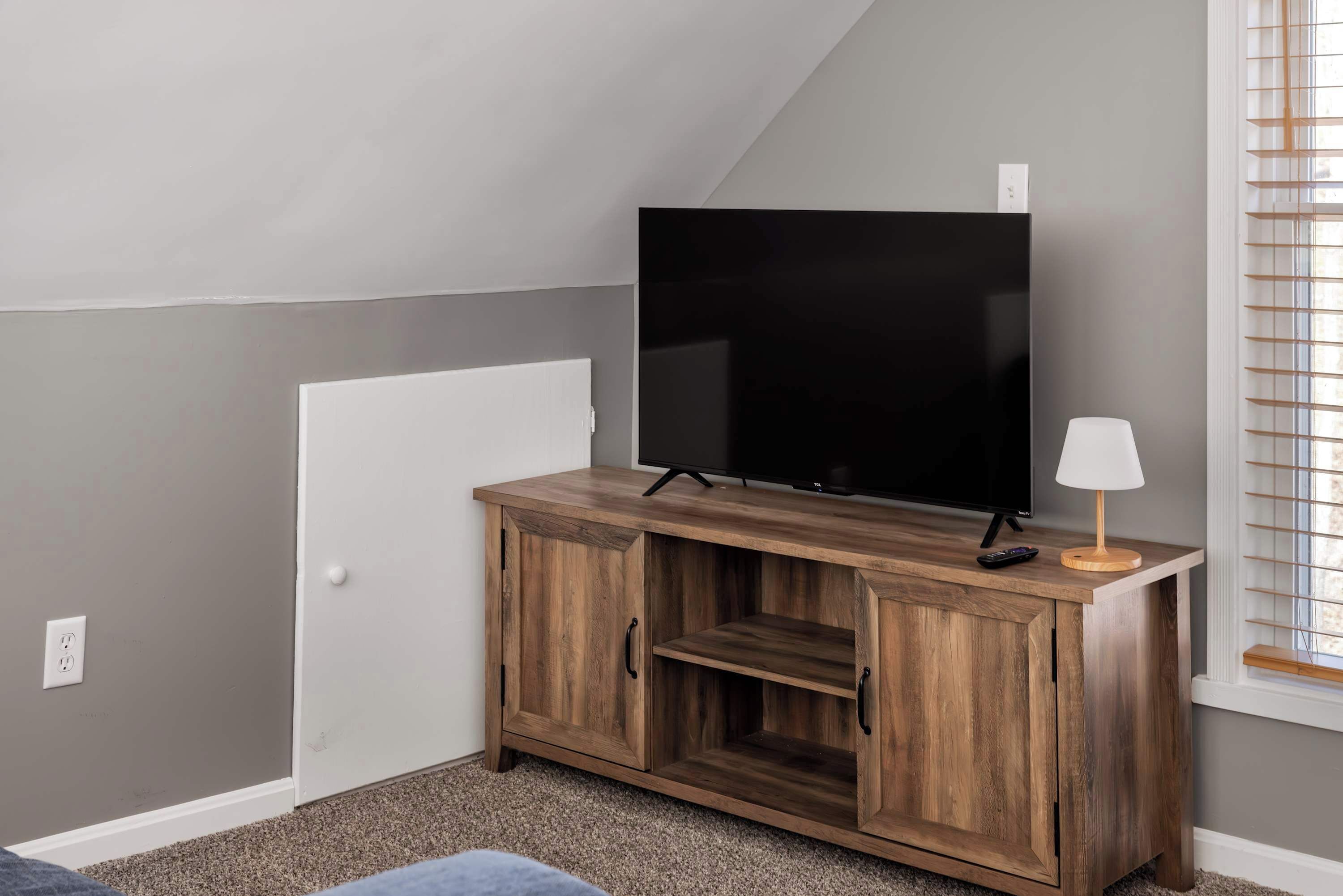 Una habitación con una televisión sobre un mueble de madera, una lámpara y una ventana con persianas.