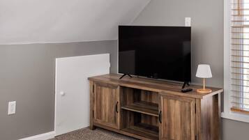 Una habitación con una televisión sobre un mueble de madera, una lámpara y una ventana con persianas.