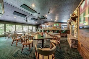Un restaurante con varias mesas y sillas, una zona de bar y una pantalla de televisión.