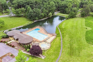 A large outdoor swimming pool surrounded by a well-maintained lawn and a small pond. - Fireplace, Fire Pit, Deck, WiFi & Pool Access (Hedgesville)