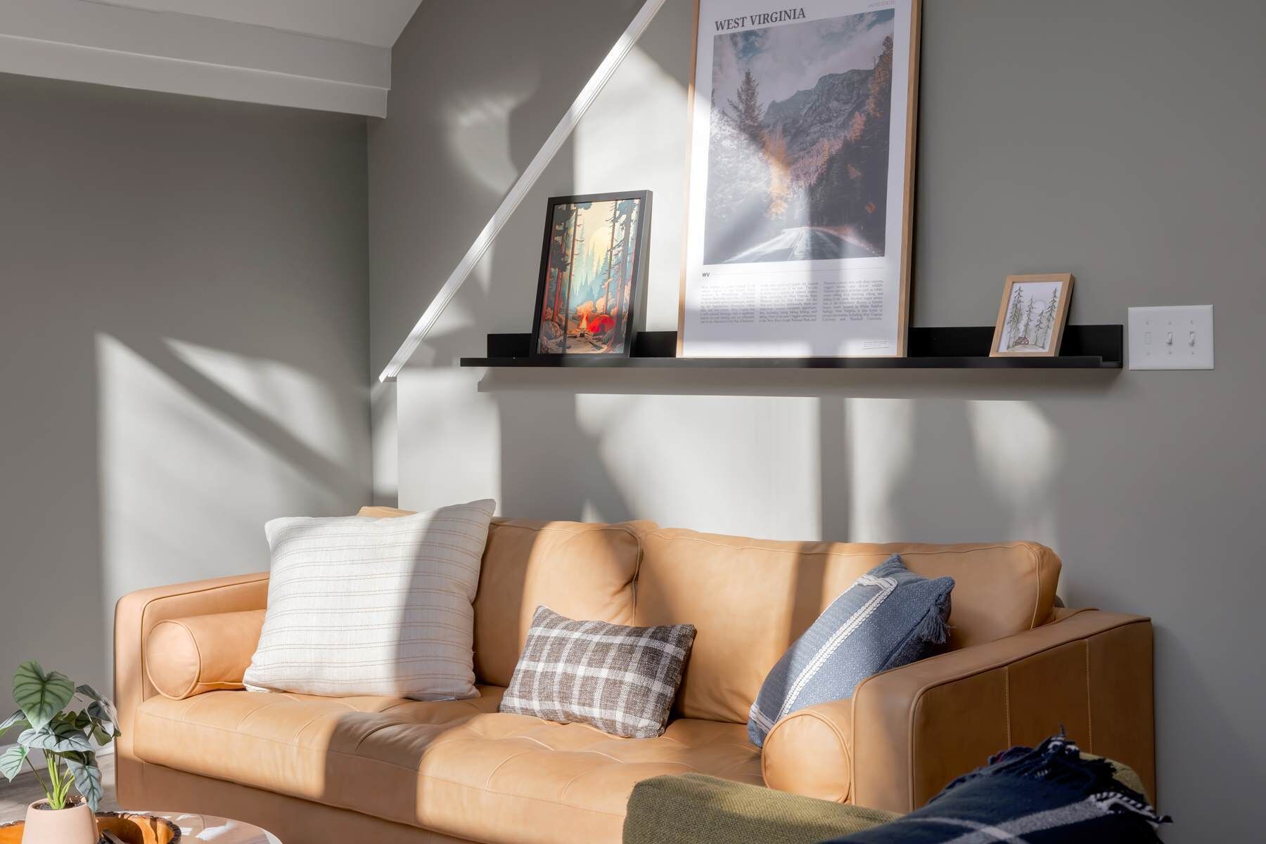 Uma sala de estar com um sofá de couro bege, um quadro emoldurado e um cartaz na parede.