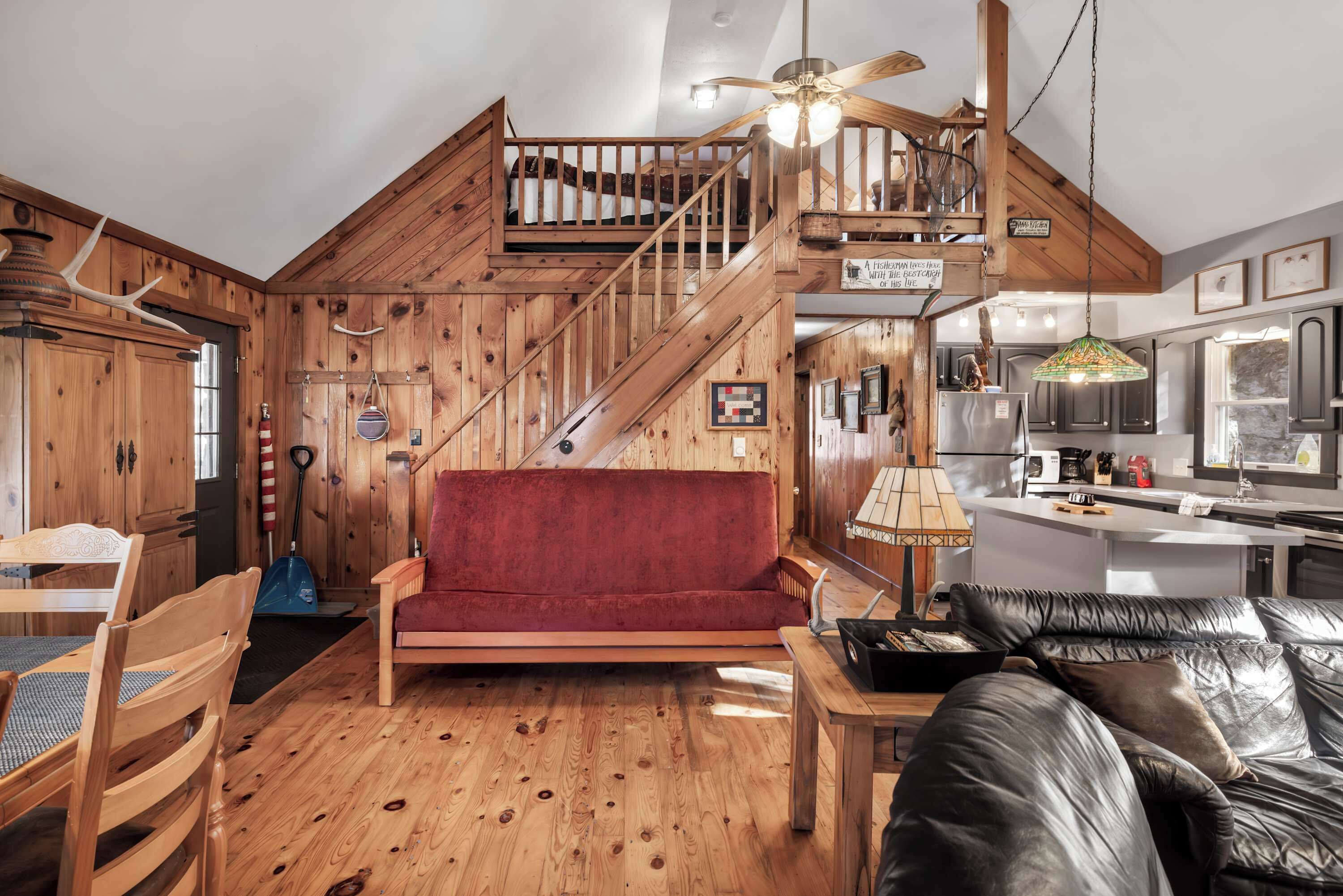 Un intérieur en bois avec un escalier, un canapé rouge, un divan en cuir noir et un coin cuisine.