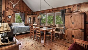 A rustic cabin interior with a bed, dining table, chairs, and a wooden cabinet. - Rustic retreat w/ kitchen & deck (Great Cacapon)