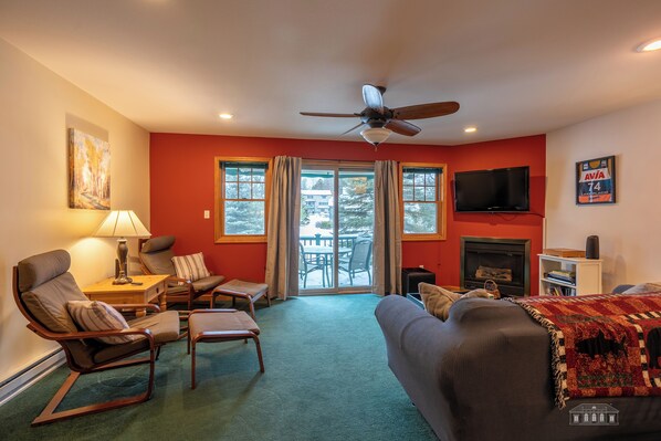 A living room with a ceiling fan, a fireplace, and a television on the wall.