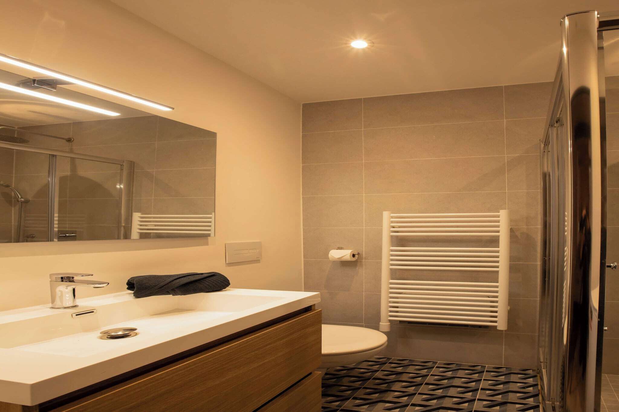 Un baño moderno con un espejo grande, un lavabo, un inodoro y una zona de ducha.