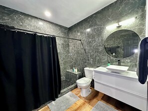 A modern bathroom with a black shower curtain, a toilet, a sink with a mirror, and a wooden floor. - The Peacock Inn  (North Las Vegas)