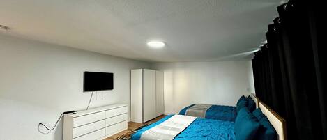 A bedroom with two beds, a TV mounted on the wall, a wardrobe, and a desk.