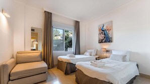 Una camera d'albergo con due letti, un divano, una grande finestra con tende e un quadro di un pavone sulla parete.