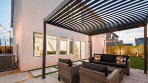 Un patio al aire libre con mobiliario de mimbre, una pérgola y luces colgantes.