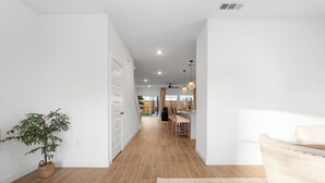 Un interior moderno con suelo de madera, paredes blancas, una zona de comedor con sillas y una mesa, y una planta en maceta.