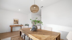 Un comedor con una mesa de madera, sillas, un florero con plantas y una lámpara colgante.