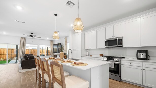 Una cocina moderna con armarios blancos, una isla central, un microondas, una estufa y un comedor con sillas y una mesa.