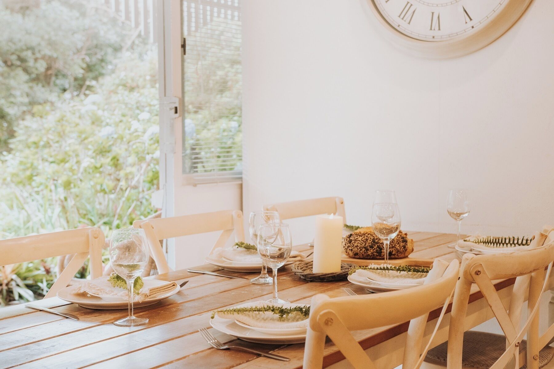A dining table set with plates, glasses, and a candle, with a clock on the wall.