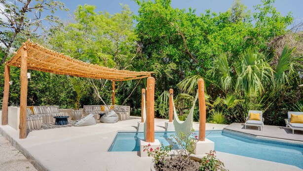 Un espace piscine agrémenté d’une pergola en bois, de sièges d’extérieur et d’un jardinier contenant un petit arbre.