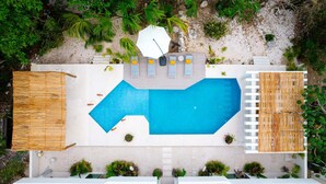 Vue aérienne d’un complexe hôtelier avec une piscine, des chaises longues et une plage.