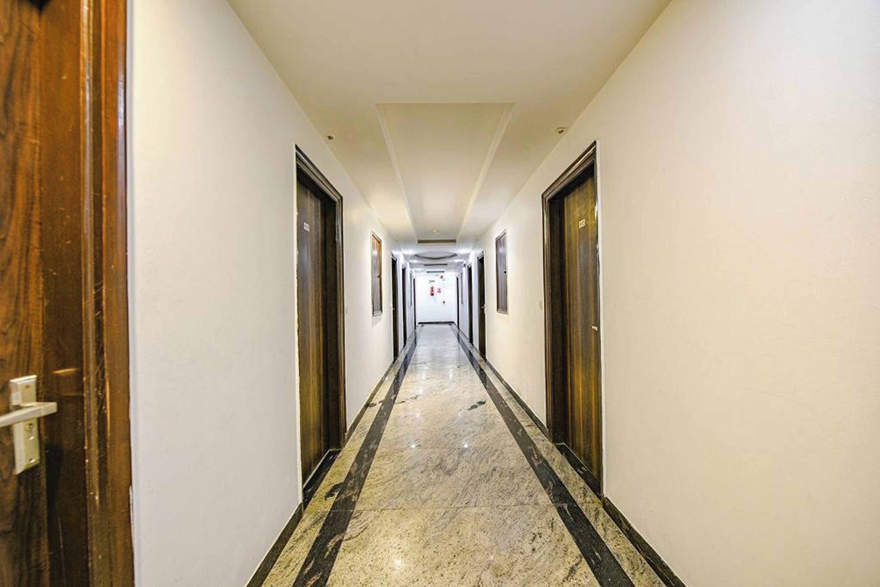 Un largo y estrecho pasillo de hotel con puertas de madera a ambos lados y suelo de mármol.