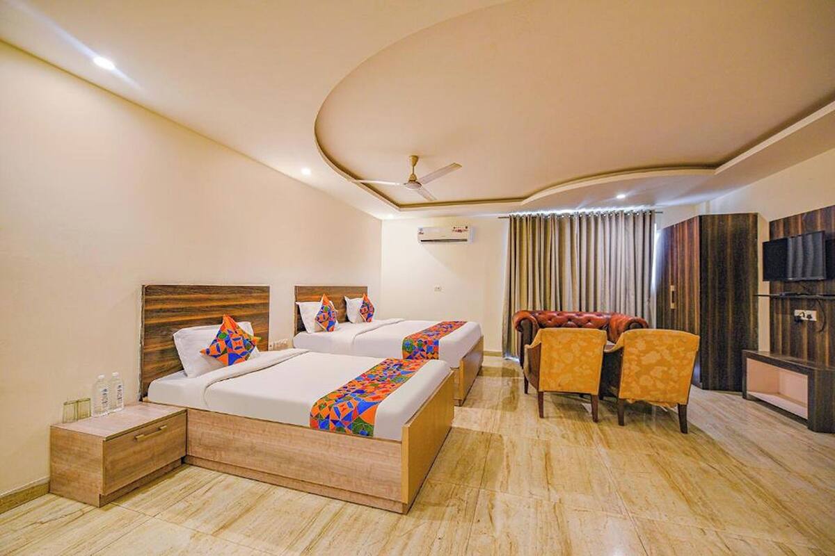 A hotel room with two beds, a desk, a chair, and a TV.
