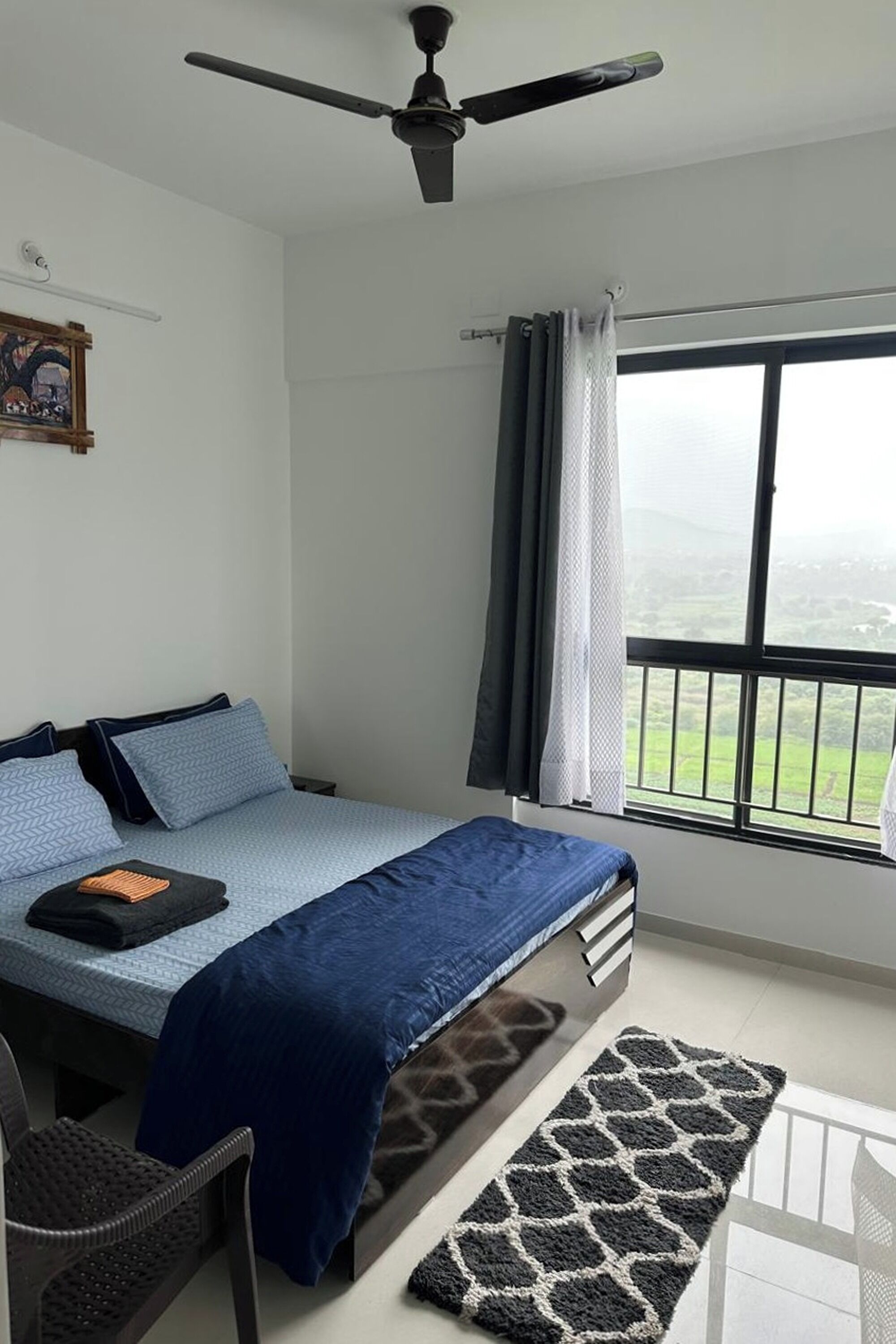 Une chambre à coucher comprenant un lit, une chaise, un bureau, une fenêtre avec vue et un ventilateur de plafond.