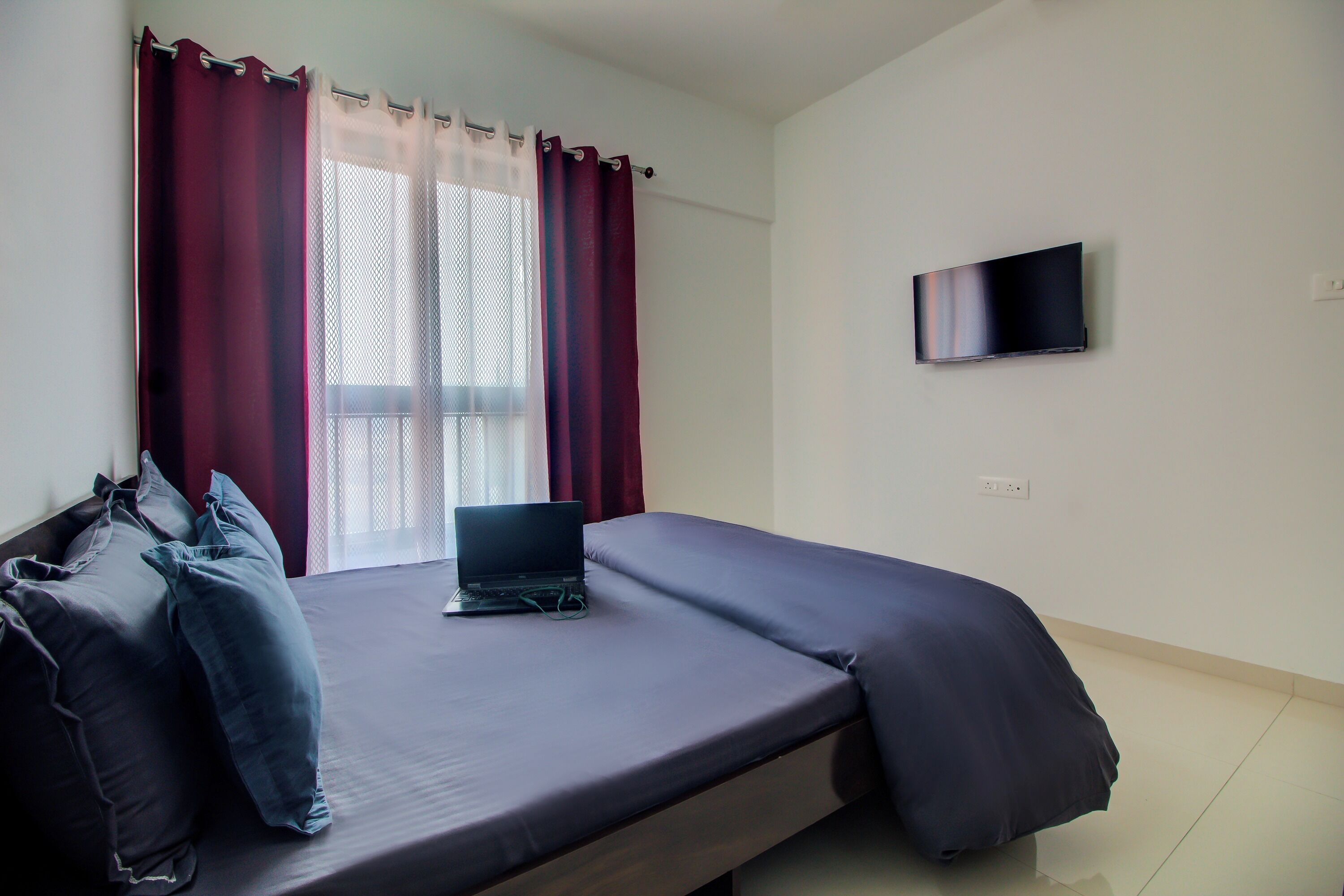 Un dormitorio con una cama, una computadora portátil y un televisor en la pared.