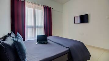 Un dormitorio con una cama, una computadora portátil y un televisor en la pared.