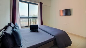 Una camera da letto con un letto, un portatile, una TV e una finestra con tende.