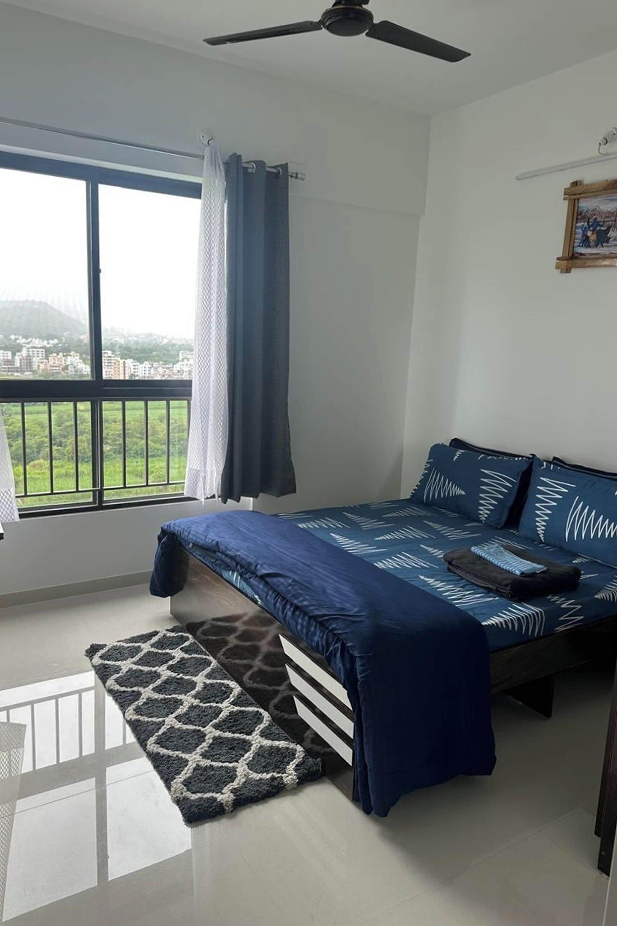 Una camera da letto con un letto, vista sulla città, ventilatore a soffitto e finestra con tende.