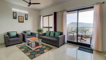 Relax in this stylish living room with a sofa set, coffee table, and vibrant rug, offering a sliding door to a balcony with a scenic mountain view.