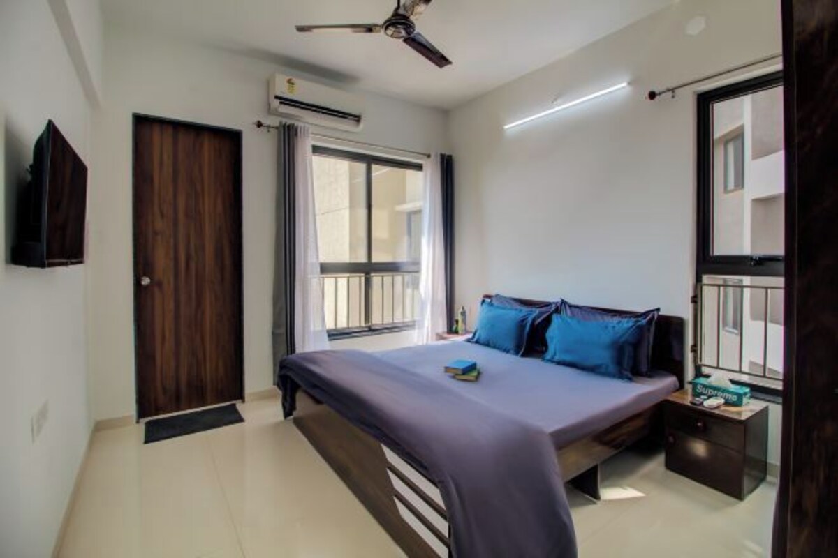 Une chambre à coucher comprenant un lit, une table de chevet, un ventilateur de plafond, une fenêtre et un appareil de climatisation.