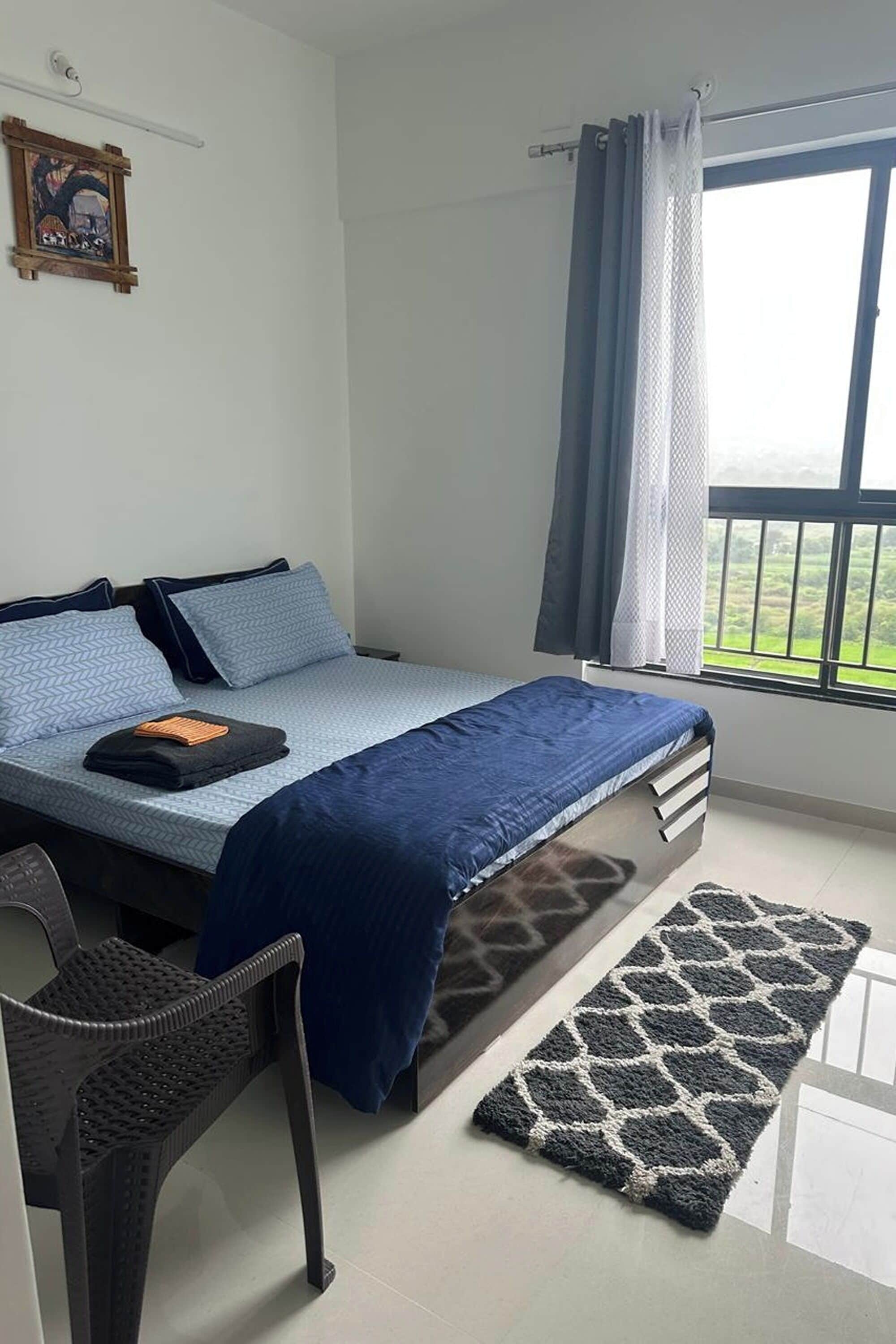 Un dormitorio con cama, una silla, una ventana con cortinas y un cuadro en la pared.