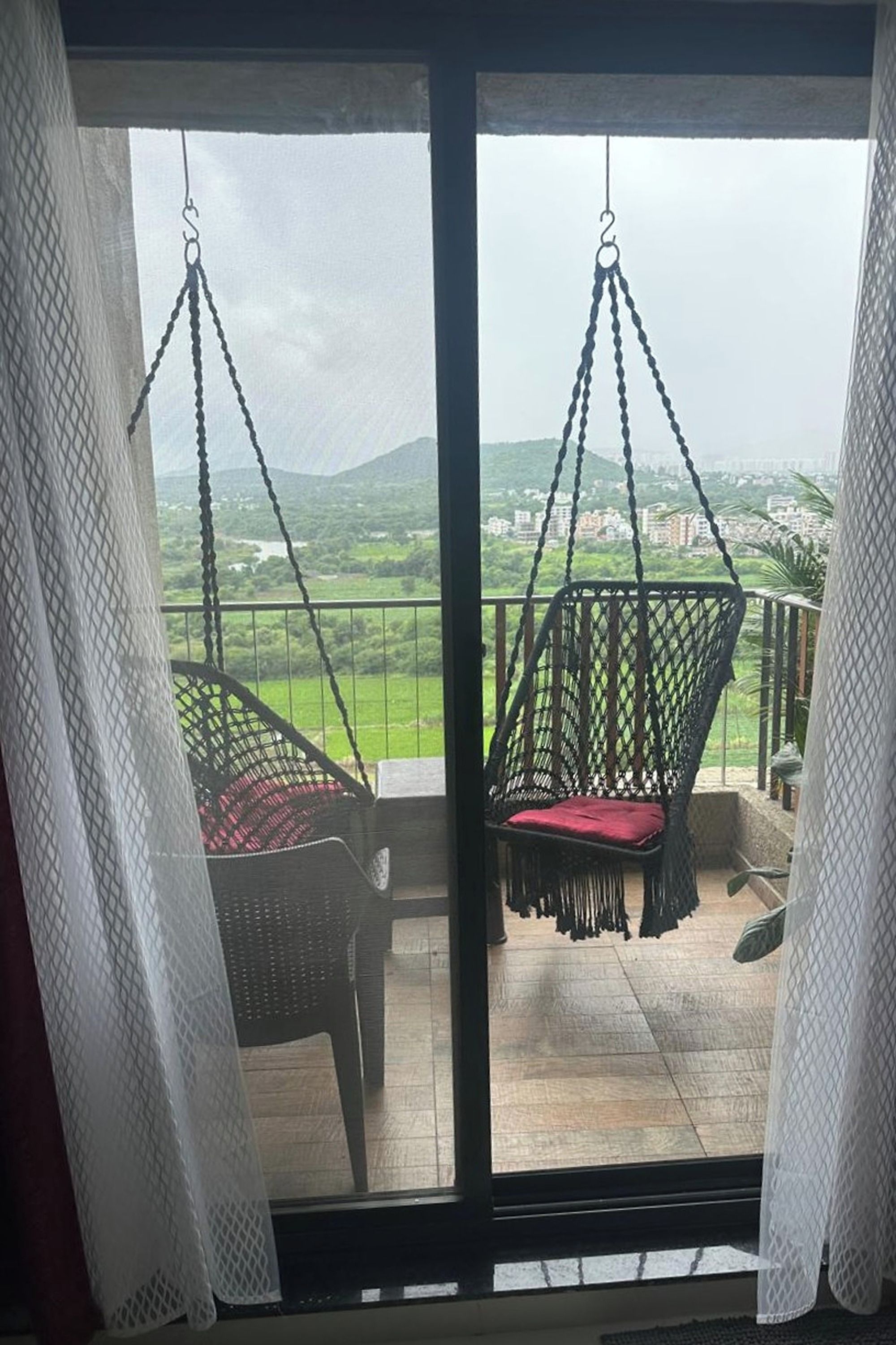 A balcony with two hanging chairs and a view of a green landscape.