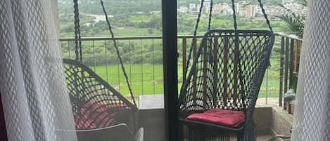 A balcony with two hanging chairs and a view of a green landscape.