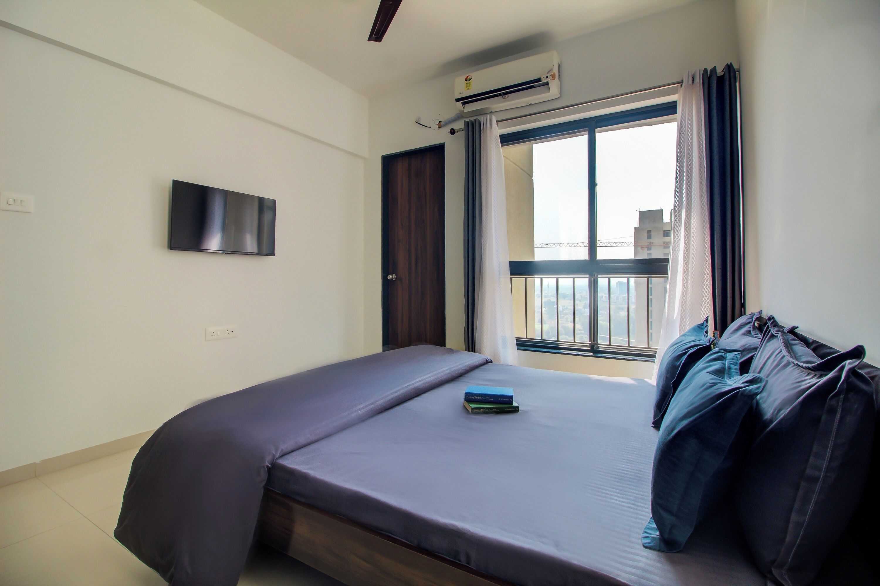 Une chambre à coucher avec un lit, un téléviseur fixé au mur et une fenêtre avec des rideaux.