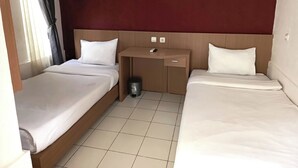 A hotel room with two single beds, a wooden desk, and a trash bin. - Khanza Costel Syariah (Karangtengah)