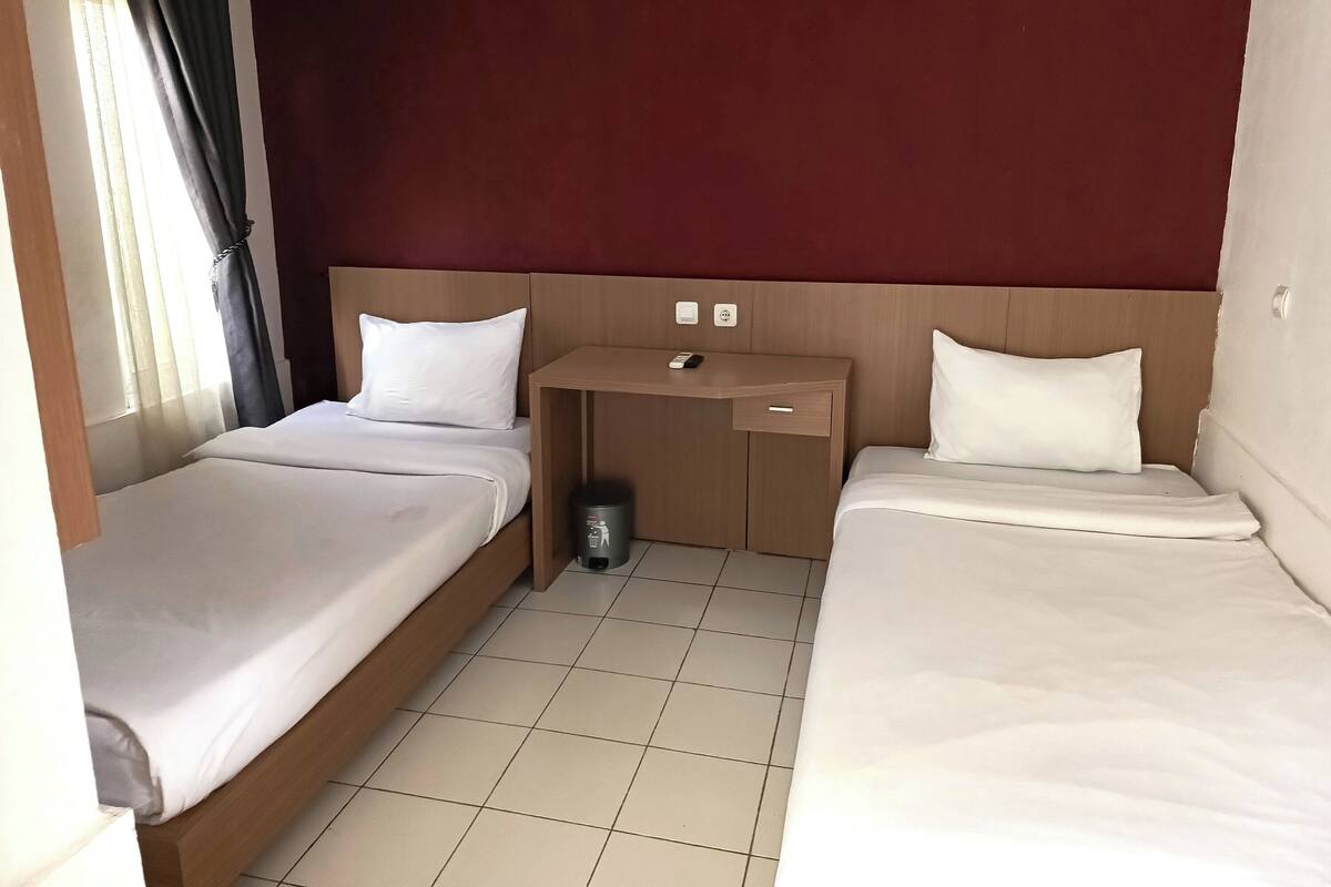 Habitación de hotel con dos camas individuales, un escritorio de madera y un cubo de basura.