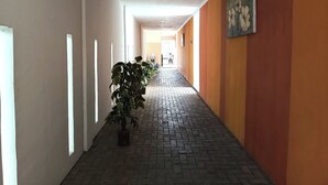 A corridor with a tiled floor, potted plants, and a painting on the wall. - Khanza Costel Syariah (Karangtengah)