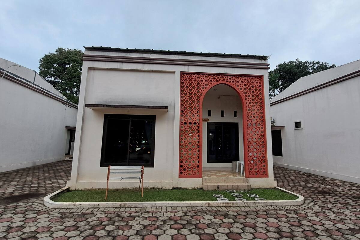 A building with a central arched entrance, a small garden area with a drying rack, and a tiled courtyard.
