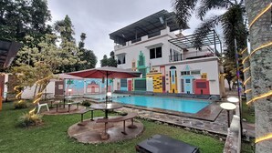 A modern building with a colorful mural, a swimming pool, outdoor seating, and a covered patio area. - Villa Zam Zam Puncak (Cisarua)