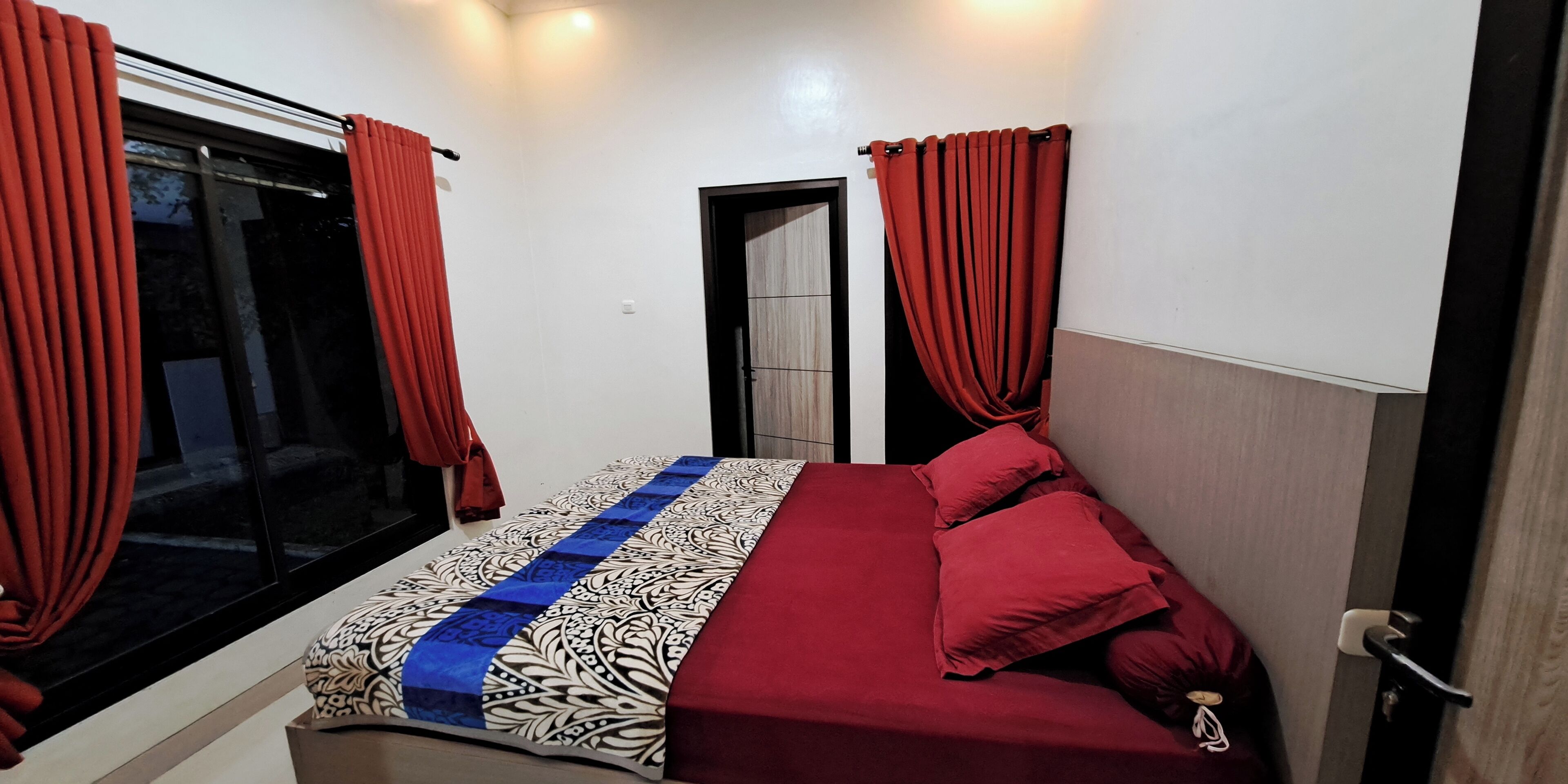 Un dormitorio con cama, cortinas rojas, una ventana y una puerta.