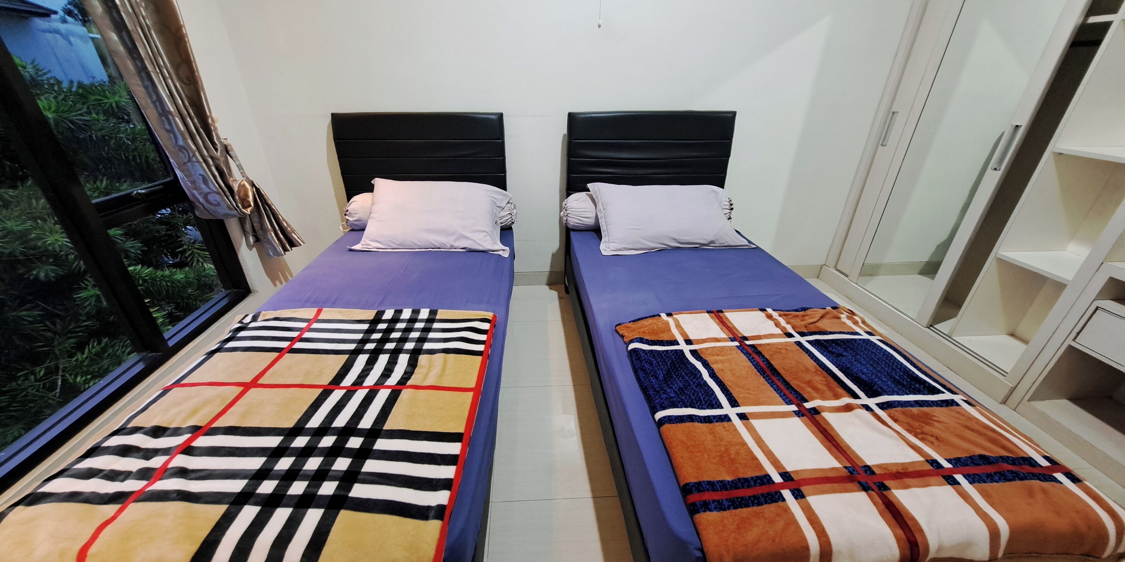Dos camas individuales con cabeceras, una ventana con cortinas y vistas al exterior.