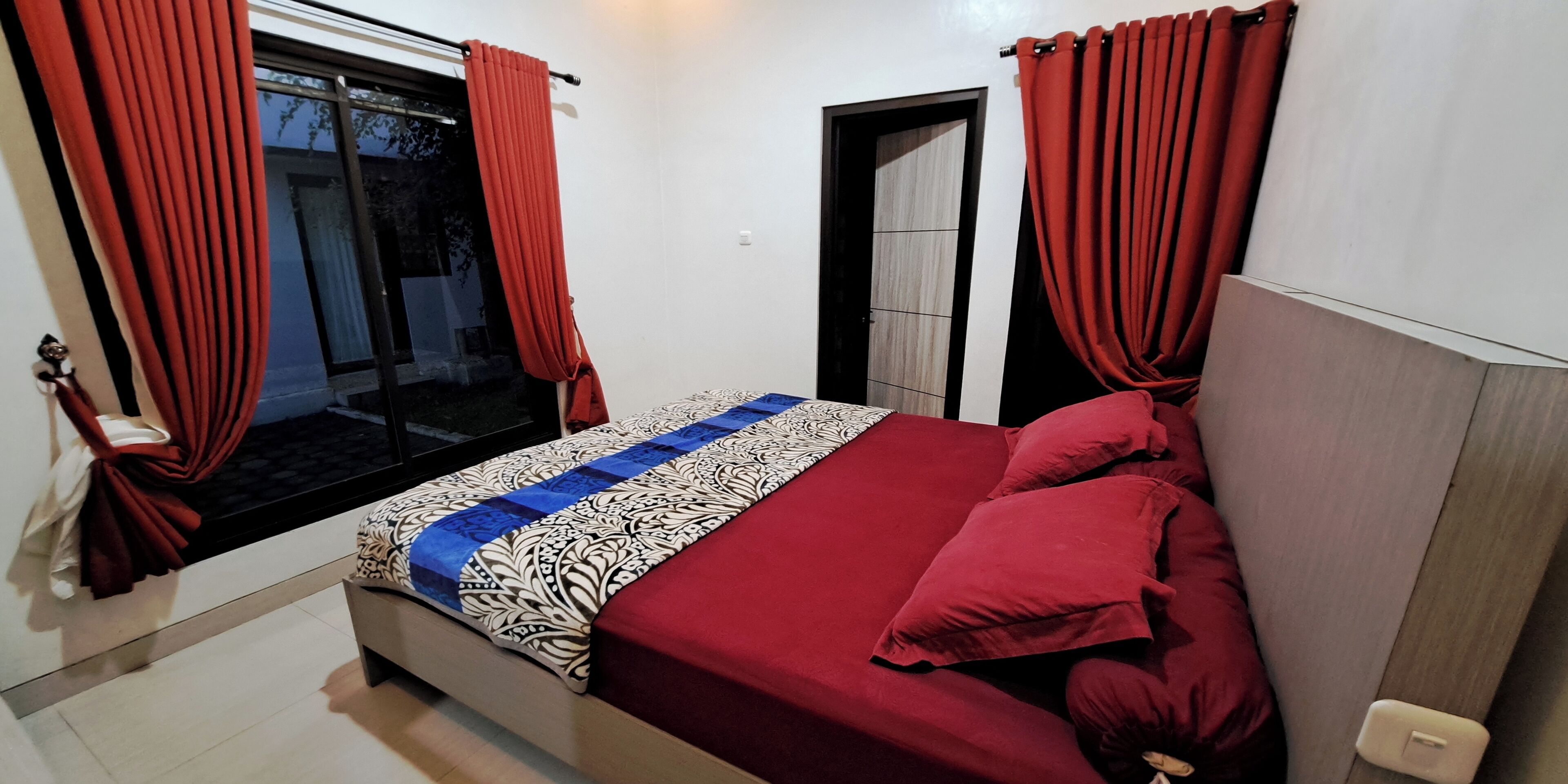 A bedroom with a bed, red curtains, a window, and a door.