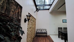 A narrow hallway with a stone wall, a wooden floor, a black metal bench, and a dining area with a table and chairs. - Villa Zam Zam Puncak (Cisarua)
