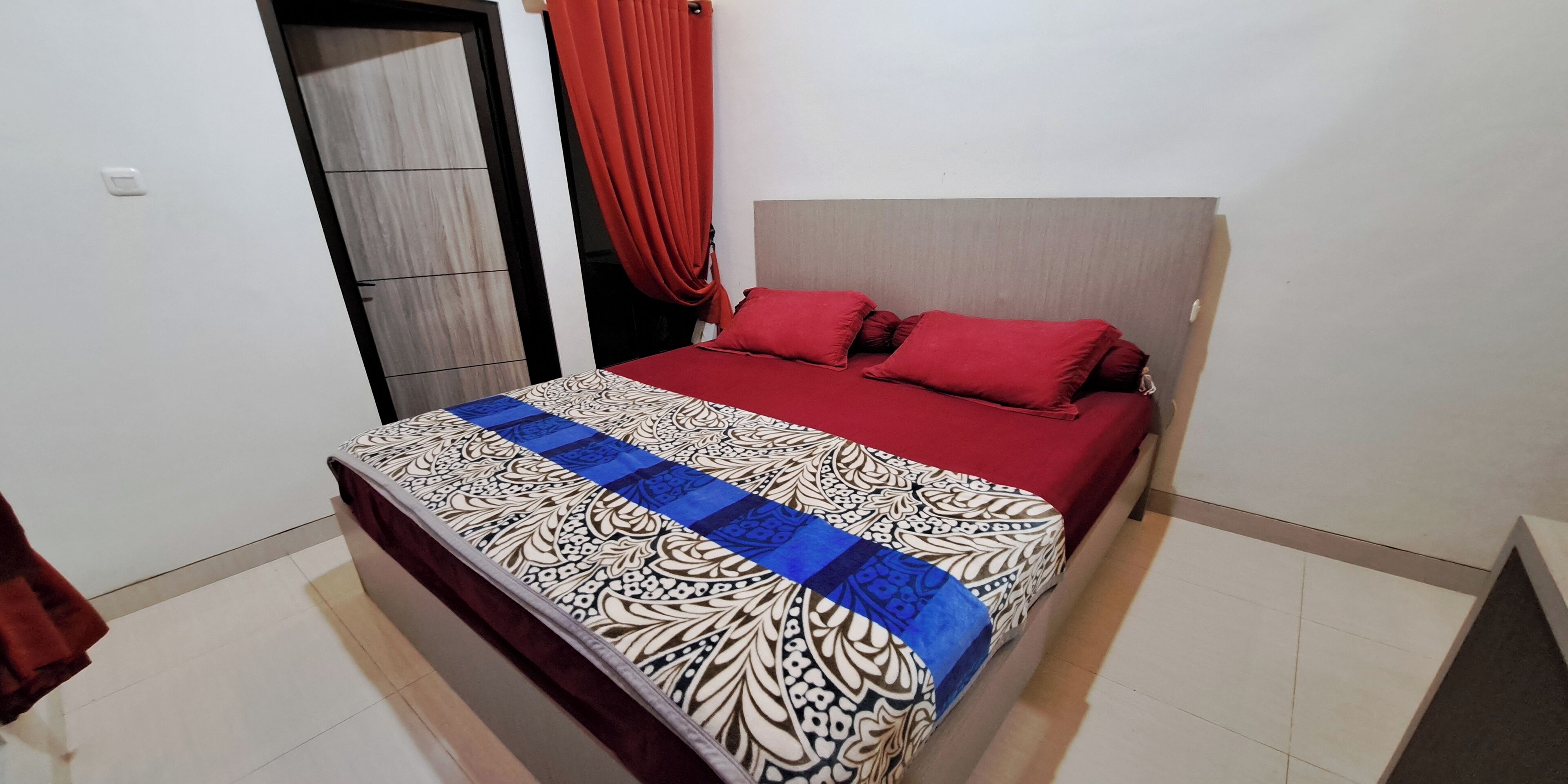 A bedroom with a bed, a red curtain, and a patterned bedspread.