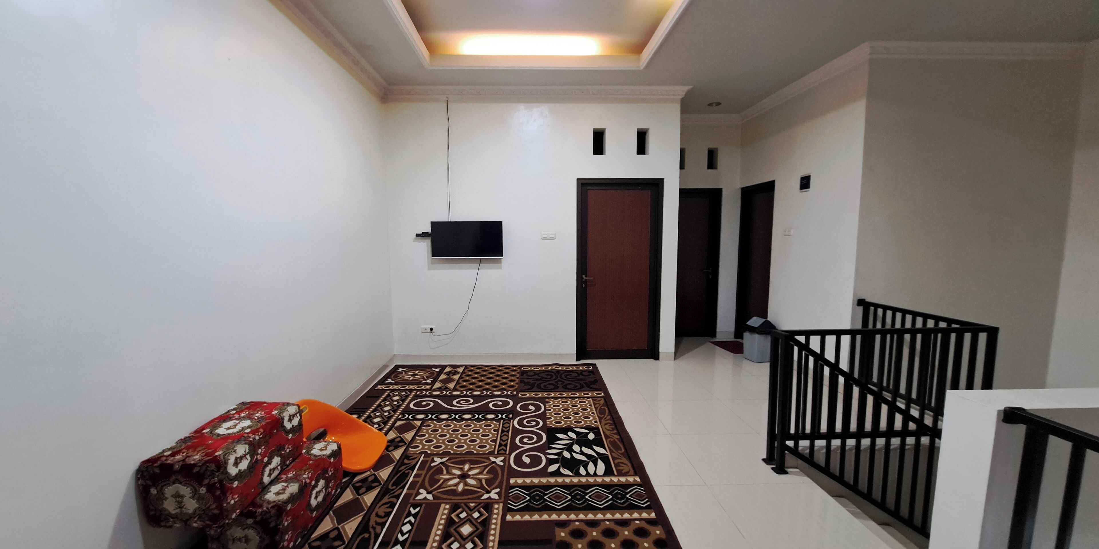 A hallway with patterned flooring, a sofa, a TV mounted on the wall, and a staircase with a black railing.