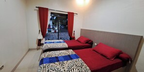 A room with two beds, a window with red curtains, and a view of the street outside. - Villa Zam Zam Puncak (Cisarua)