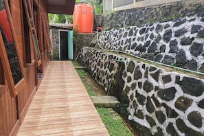 A wooden deck leading to a stone wall with a water feature. - Villa Zoya 1 (Megamendung)