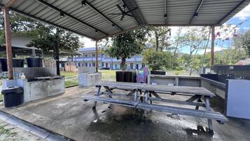 Un espacio al aire libre cubierto con una mesa de picnic, botes de basura y un dispensador de agua.