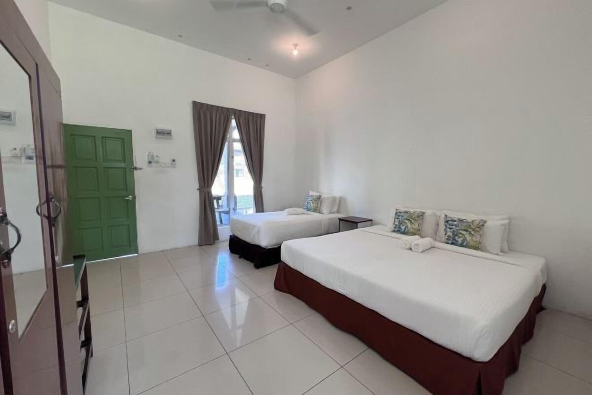 A hotel room with two beds, a green door, a window with curtains, and a ceiling fan.