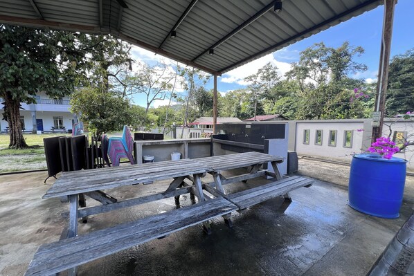 An outdoor patio area with picnic tables, a barbecue grill, and a blue barrel. - Jasa Resort Sungai Lembing (Sungai Lembing)
